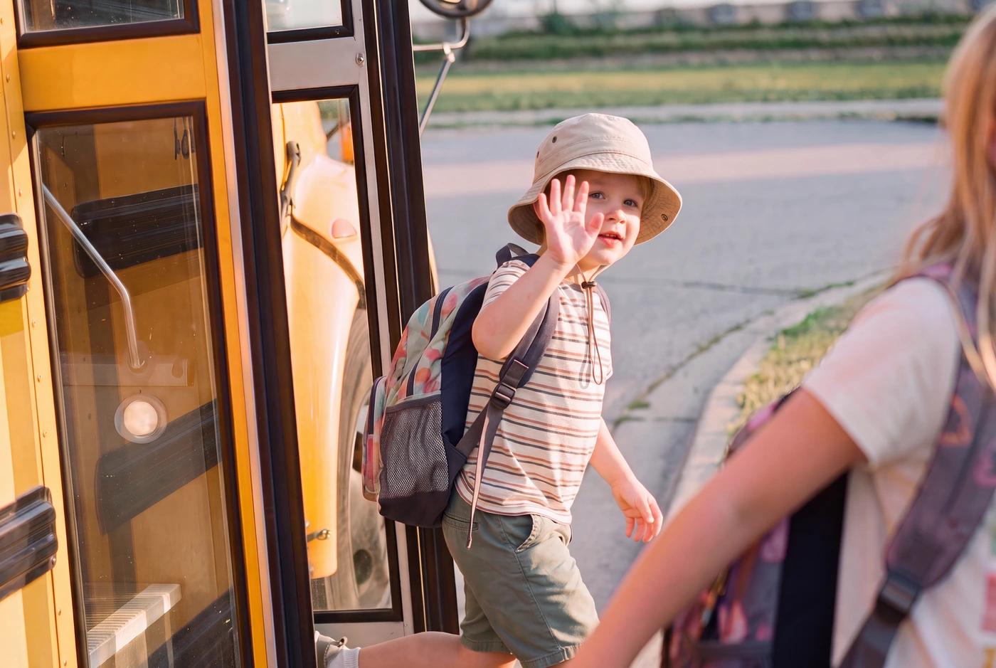 A young boy waving from the door of a yellow school bus